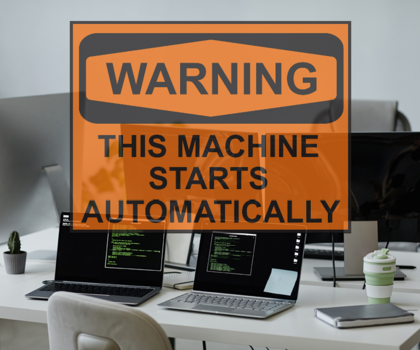 Schreibtisch mit mehreren Laptops drauf, darüber ein Schild auf dem steht "This machine starts automatically"